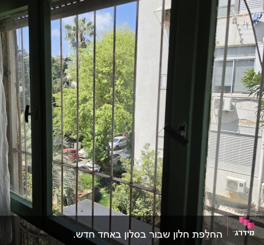 חלון עם סורגים ונוף חיצוני של עצים ובניינים